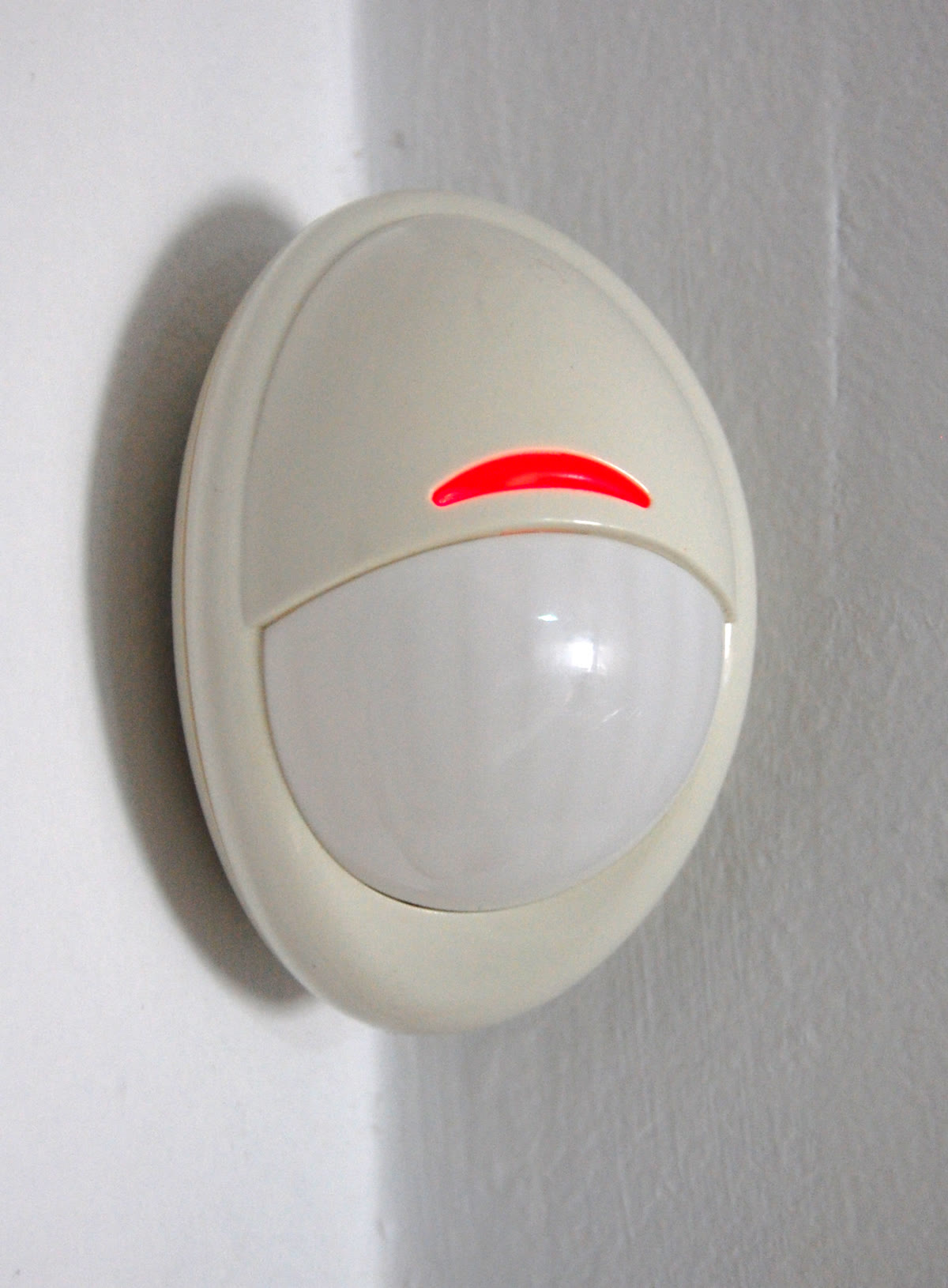 Sensor de presença do alarme preso no alto de uma parede branca, com a luz acesa